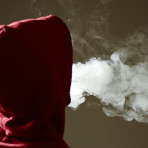 figure in a hoodie blowing smoke