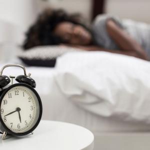 An alarm clock next to a sleeping person