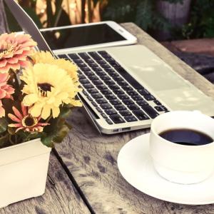 coffee cup sitting next to flowers and laptop