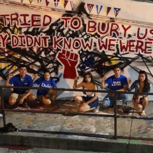 students with fists raised in front of mural