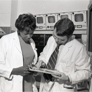 Archival image of Joyce Nichols examining a document with an unidentified physician