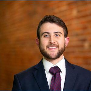 A young adult wearing a suite and tie smiles at the camera.