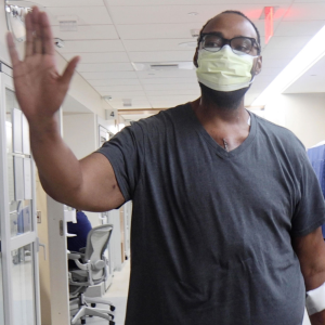 A man wearing a surgical masks high-fives a person off-camera while a woman looks on. 