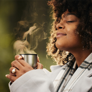 Curly haired Black woman enjoying the scent from a steaming mug. 