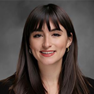 Headshot of Kayla Corredera-Wells smiling at camera with long brown straight hair and bangs falling in front of shoulders over black shirt