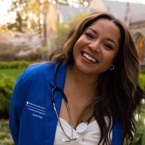 Carlita smiling in her blue OT doctor coat outside Duke Chapel