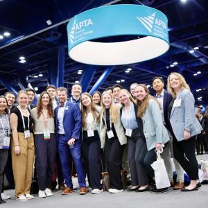 more than a dozen students and faculty posing for a group photo on the floor of the APTA CSM conference