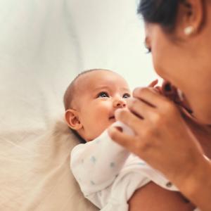 A smiling woman gently grasps hands with a baby who smiles back up at her
