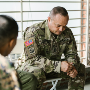Two military personnel in uniform are seated and engaged in a discussion
