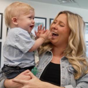A woman smiles at a young boy she's holding as he laughs and claps his hands