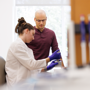 Jonathan Campbell with a gloved lab member watching her perform an experiment.