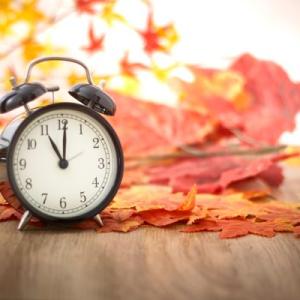 Alarm clock surrounded by orange autumn leaves